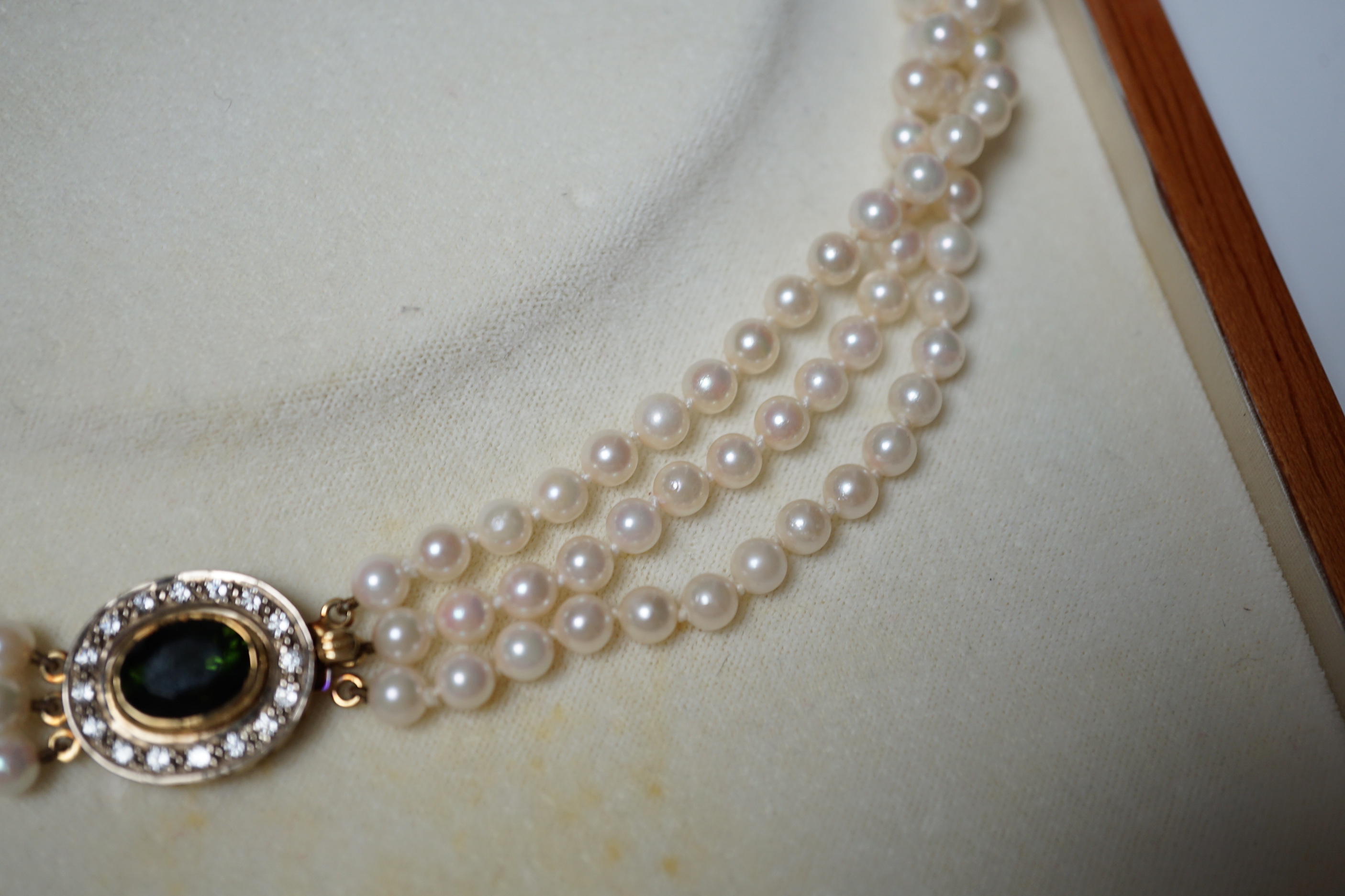 A modern triple strand cultured pearl necklace, with green tourmaline and diamond cluster set oval yellow metal clasp, 48cm.